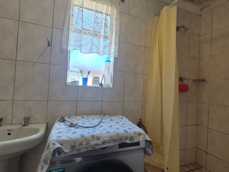 A functional bathroom featuring a pedestal basin, shower area, and tiled finishes, currently serving as a combined laundry space.