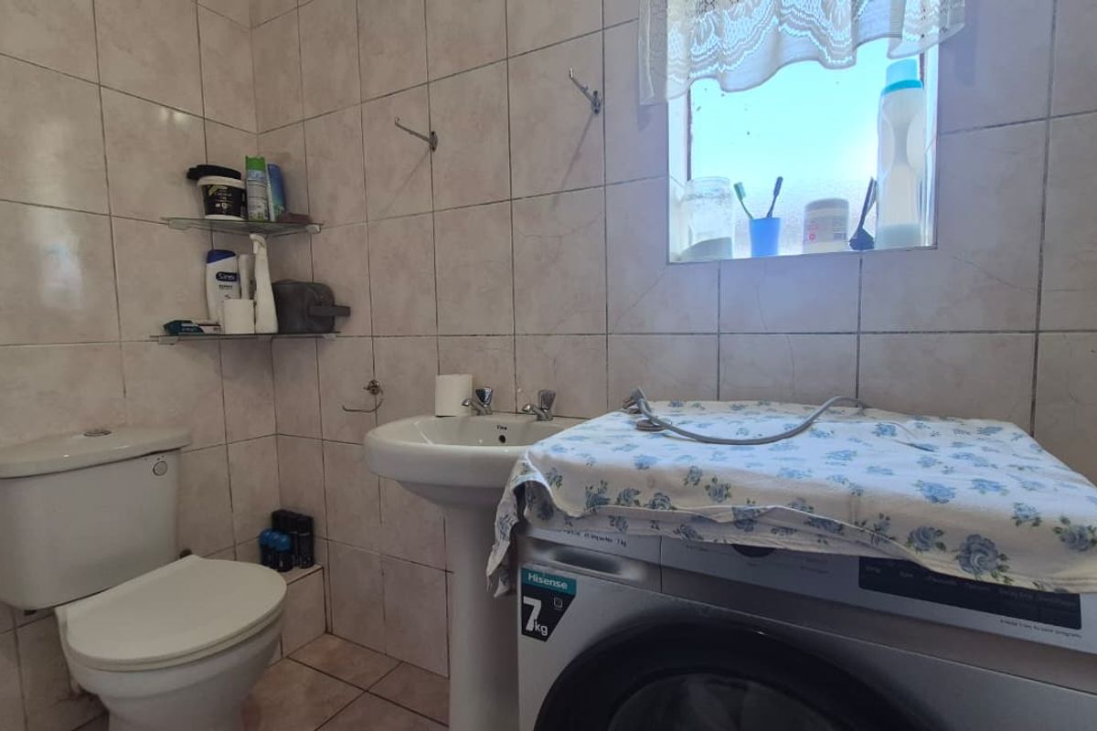 A functional bathroom featuring a pedestal basin, toilet, and fully tiled walls and floors, providing a practical and easy-to-maintain space.