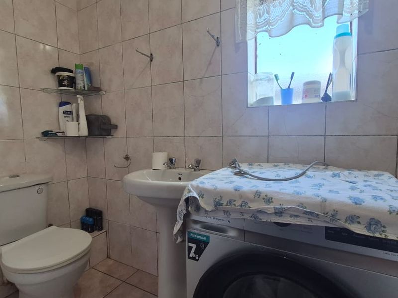 A functional bathroom featuring a pedestal basin, toilet, and fully tiled walls and floors, providing a practical and easy-to-maintain space.