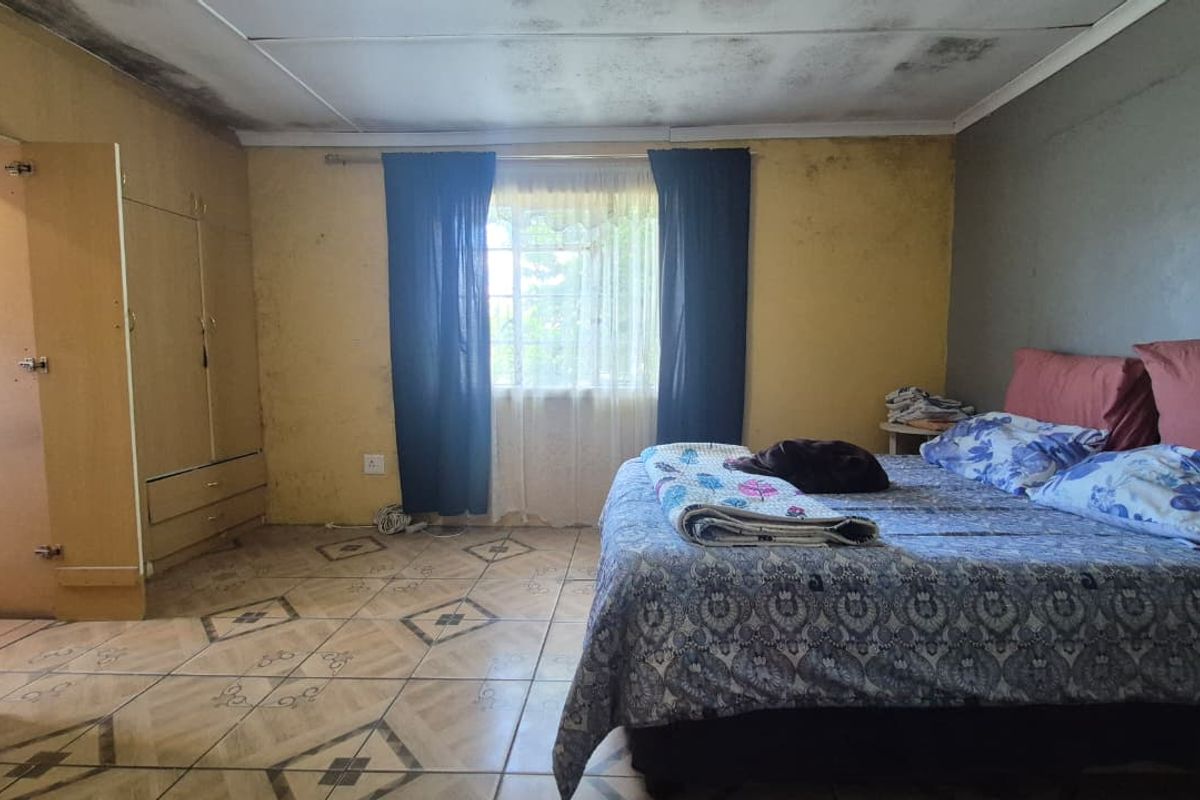 A bedroom featuring built-in cupboards and tiled flooring, currently requiring significant maintenance and cosmetic repairs to the ceiling and walls.