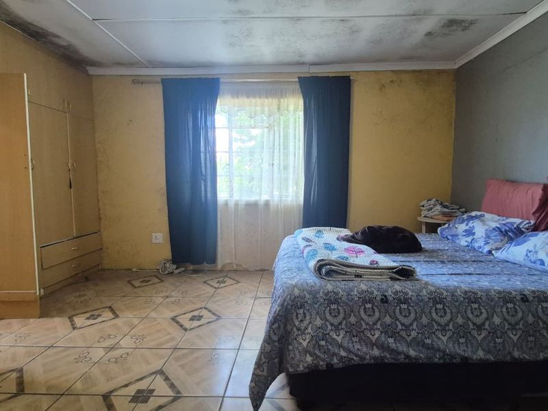 A bedroom featuring built-in cupboards and tiled flooring, currently requiring significant maintenance and cosmetic repairs to the ceiling and walls.