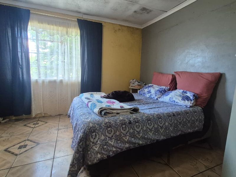 A bedroom featuring tiled flooring and a window with security bars, currently showing signs of wear on the walls and ceiling.
