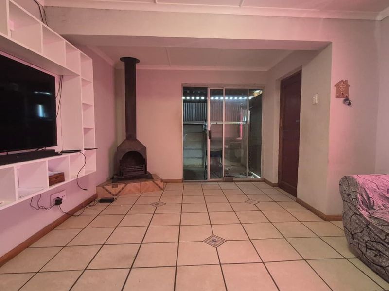 Living room featuring tiled flooring, a built-in shelving unit, and a freestanding fireplace with access to an outdoor area via a sliding glass door.