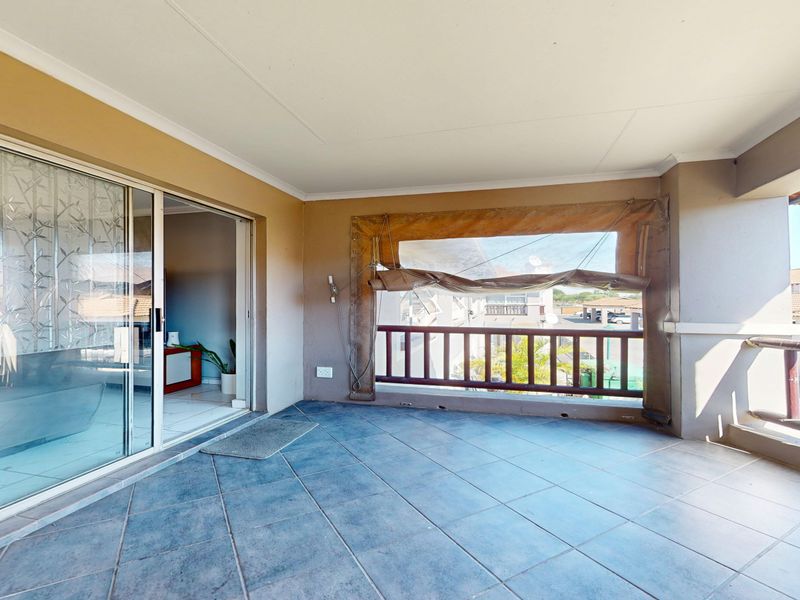 A spacious covered balcony featuring tiled flooring, a wooden balustrade, and a sliding glass door providing access to the interior living area.