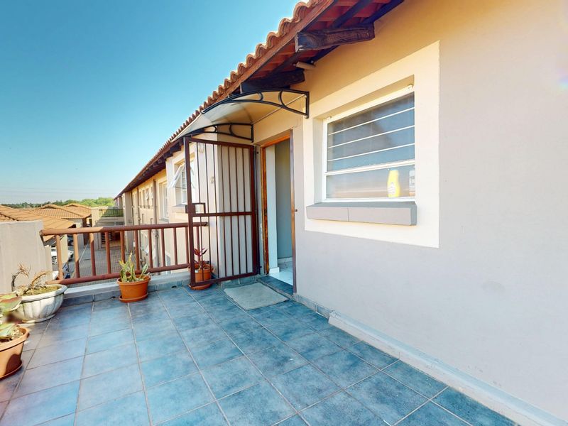 An open balcony area featuring tiled flooring, a protective awning, and a metal security gate, providing outdoor space for the apartment.