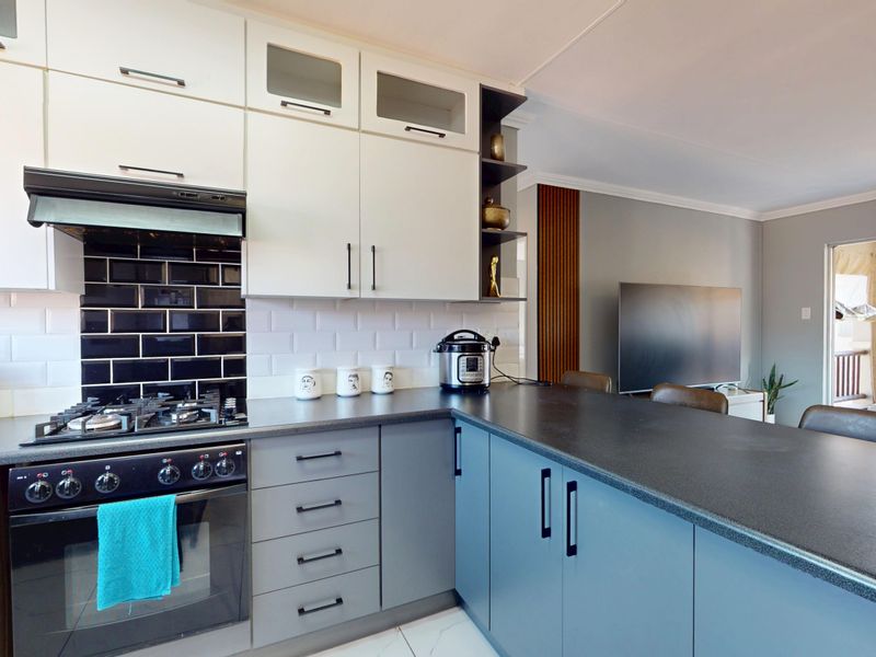 Modern open-plan kitchen featuring two-tone cabinetry, subway tile backsplash, gas hob, and a functional breakfast bar overlooking the living area.