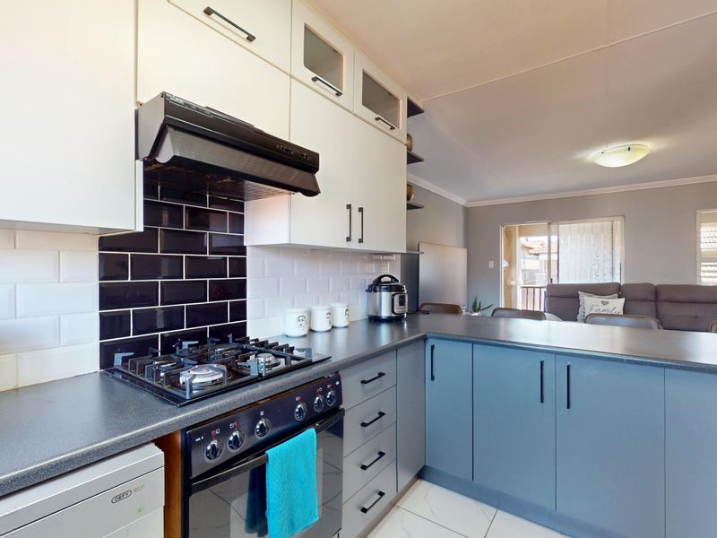 Modern open-plan kitchen featuring a gas hob, built-in oven, extractor fan, subway tile backsplash, and ample cabinetry, seamlessly flowing into the living area.