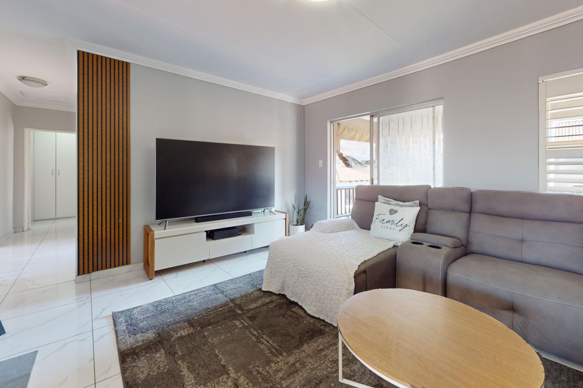 A bright living room featuring modern tiled flooring, decorative timber wall paneling, and a sliding glass door leading to an outdoor area.