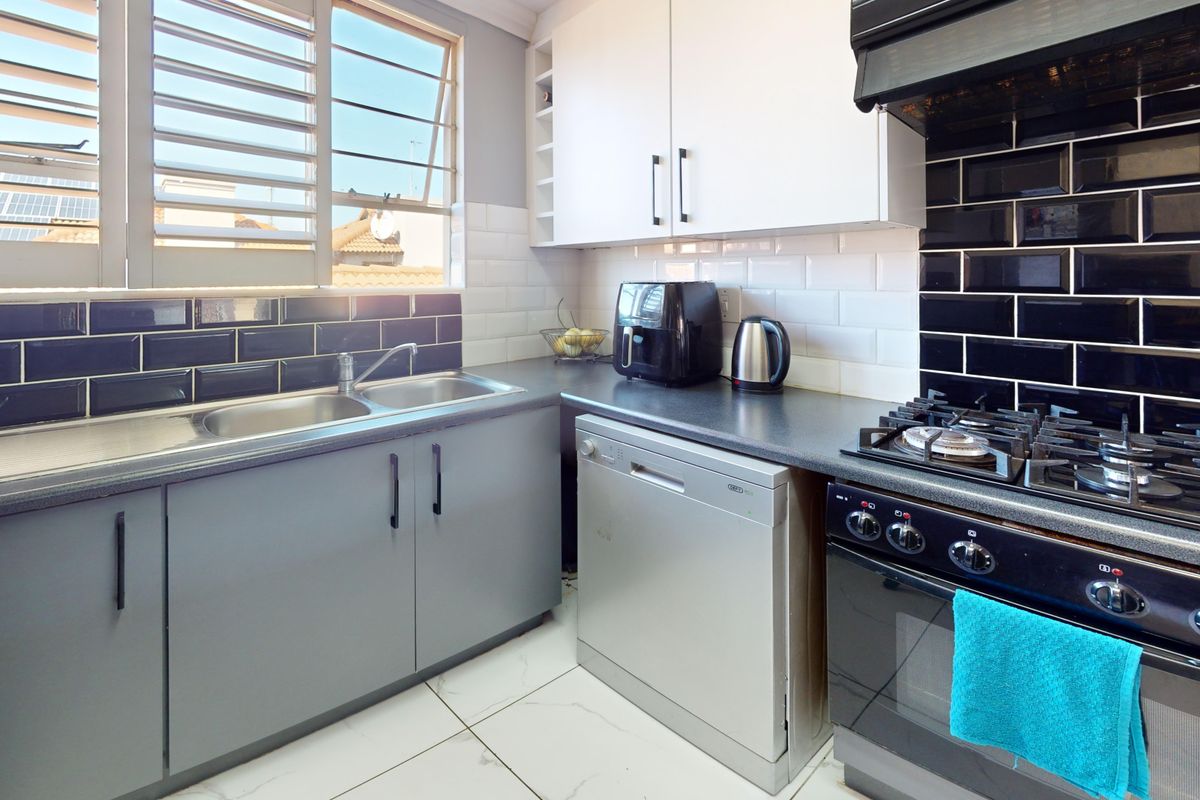 A functional kitchen featuring dark countertops, white and grey cabinetry, a gas hob with extractor, and a double sink with louvered windows.