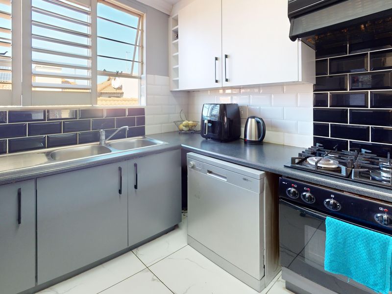 A functional kitchen featuring dark countertops, white and grey cabinetry, a gas hob with extractor, and a double sink with louvered windows.