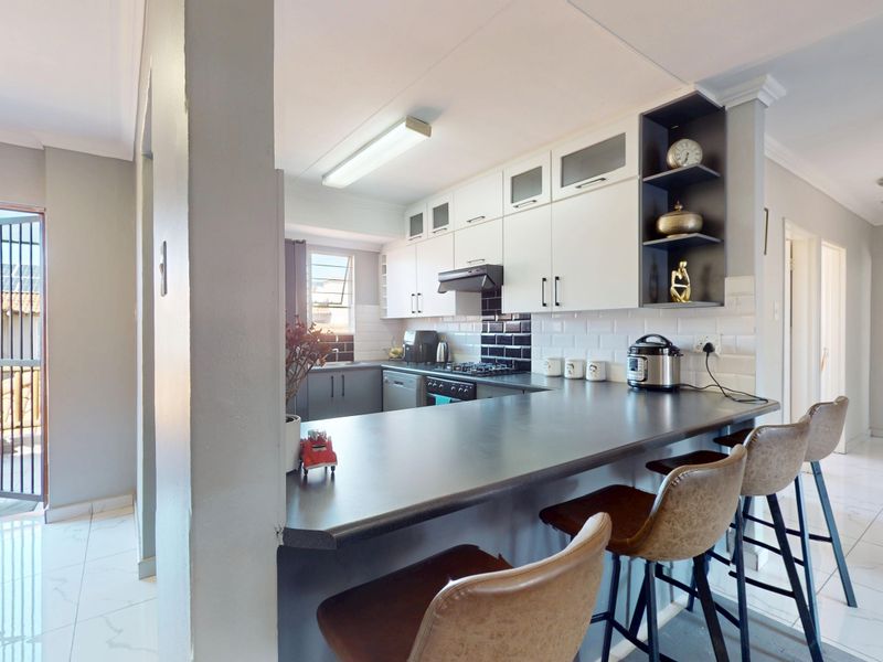 Open-plan kitchen featuring a breakfast bar, modern cabinetry, subway tile backsplash, and tiled flooring, with direct access to an outdoor balcony area.