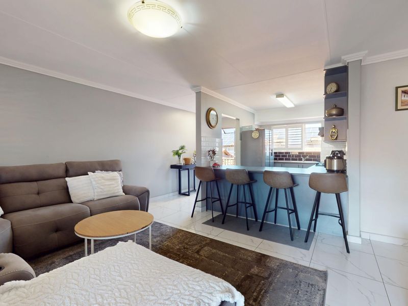 An open-plan living and kitchen area featuring a breakfast bar, tiled flooring, and built-in cabinetry, creating a functional and connected living space.