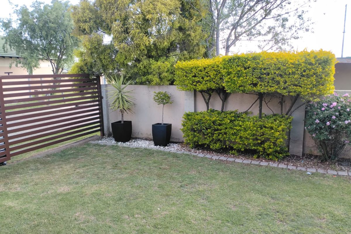 A well-maintained private garden area featuring a neat lawn, established hedging, and a modern slatted metal boundary fence.