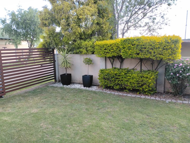 A well-maintained private garden area featuring a neat lawn, established hedging, and a modern slatted metal boundary fence.