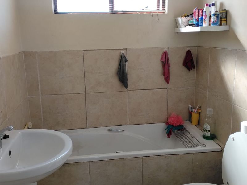 A functional bathroom featuring a pedestal basin, built-in bathtub, and ceramic tiling throughout, providing a standard layout with natural light from the window.