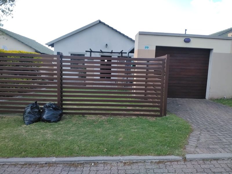 Front view of a residential property featuring a horizontal slat fence, a single garage with a paved driveway, and a small front lawn.
