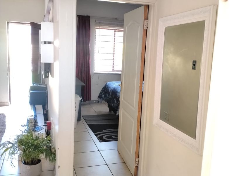 A view through a hallway connecting to a bedroom, featuring tiled flooring and neutral wall finishes.