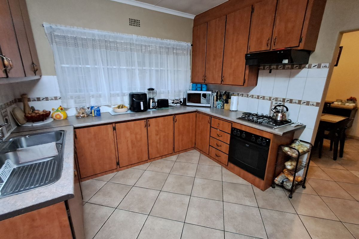 A functional kitchen featuring wooden cabinetry, laminate countertops, a gas hob, built-in oven, and tiled flooring with a neutral backsplash.