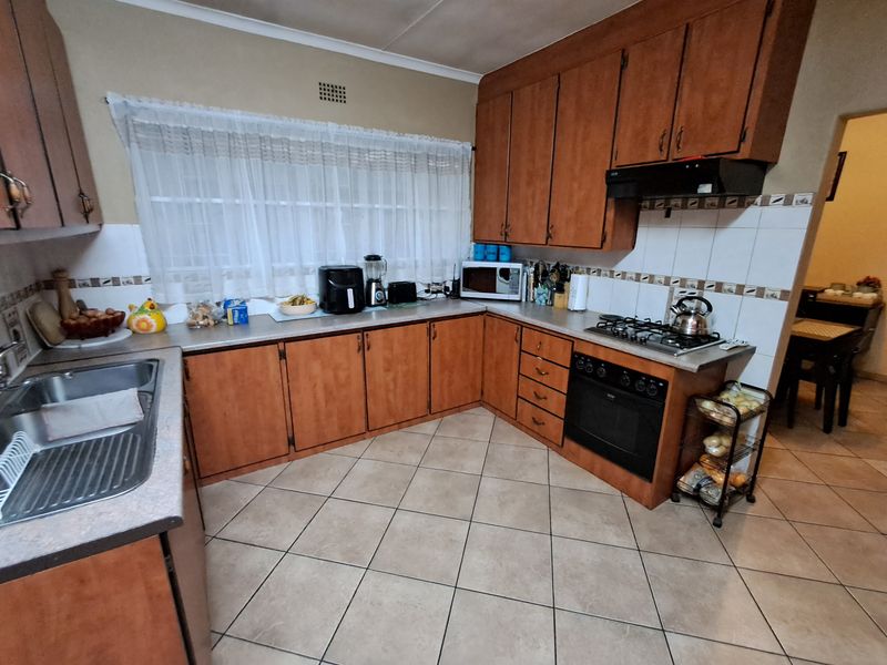 A functional kitchen featuring wooden cabinetry, laminate countertops, a gas hob, built-in oven, and tiled flooring with a neutral backsplash.