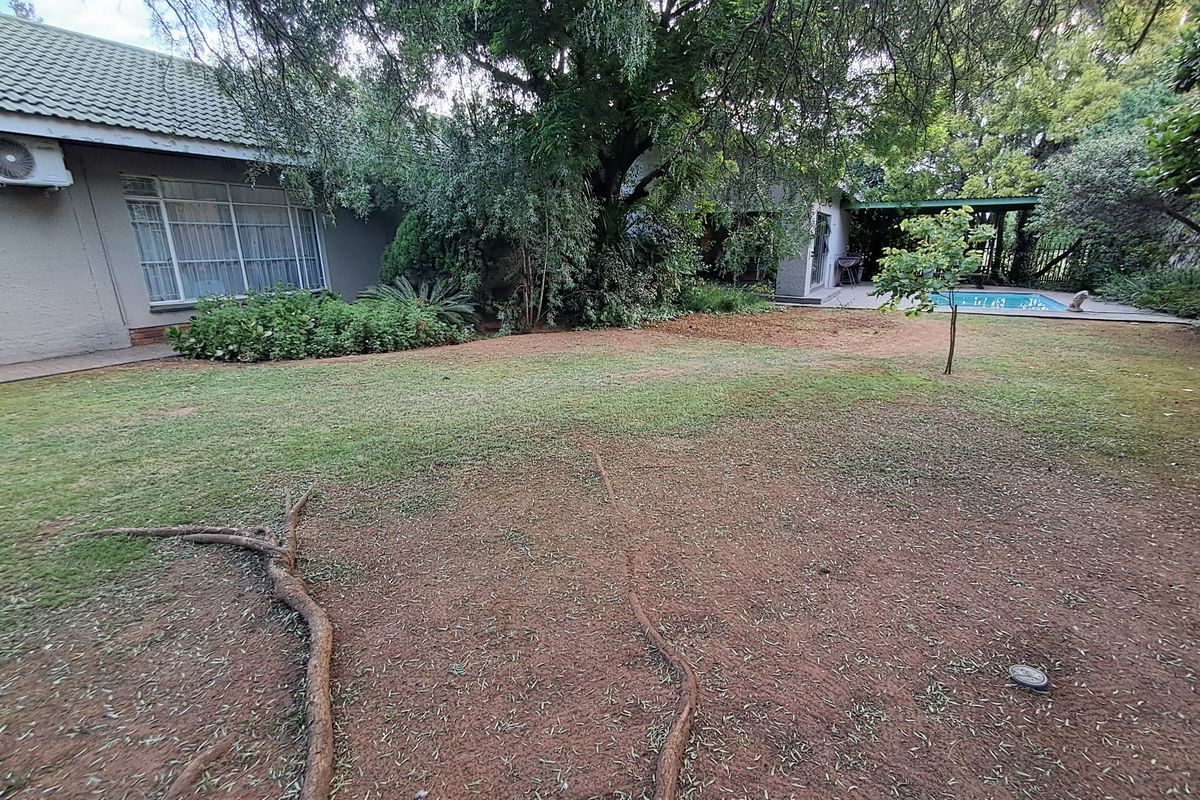 Spacious rear garden featuring a swimming pool, mature trees, and a covered patio area adjacent to the main house structure.