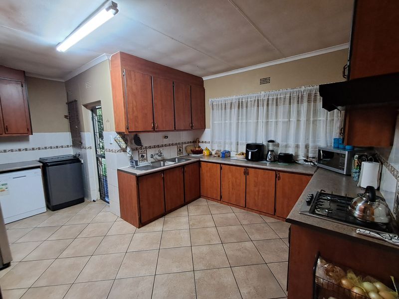 A functional kitchen featuring built-in wooden cabinetry, laminate countertops, a gas hob, and tiled flooring, offering a practical layout with potential for modern updates.