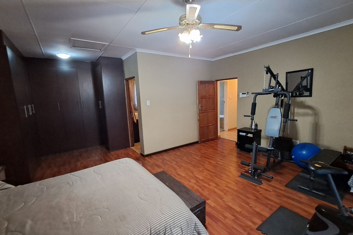 Spacious bedroom featuring dark wood built-in cupboards, laminate flooring, and a ceiling fan, with an adjoining en-suite bathroom.