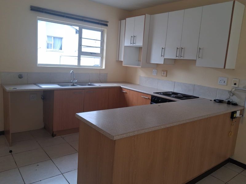 A functional kitchen featuring wood-finish cabinetry, laminate countertops, a built-in electric hob, and tiled flooring, offering a clean and practical workspace.