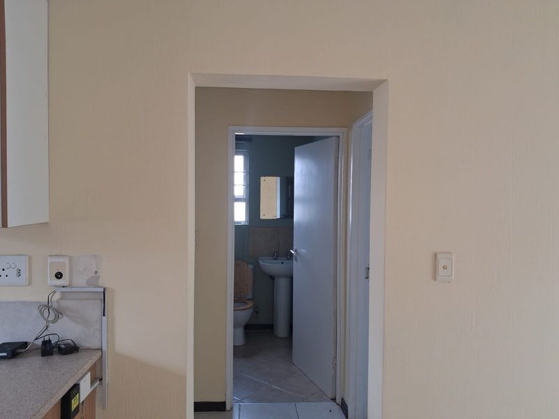 A view from a kitchen area looking into a small bathroom featuring a pedestal basin and toilet with tiled flooring.