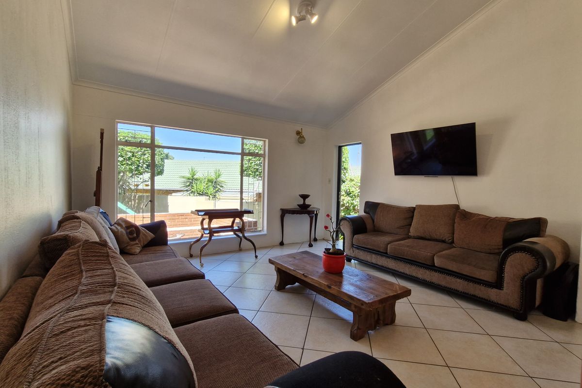 Spacious living room featuring tiled flooring, a vaulted ceiling, and a large window providing natural light and garden views.