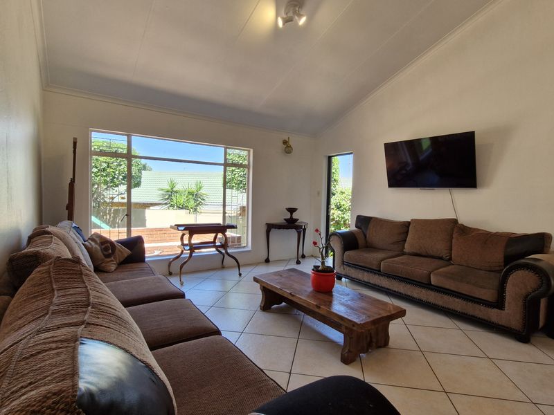 Spacious living room featuring tiled flooring, a vaulted ceiling, and a large window providing natural light and garden views.