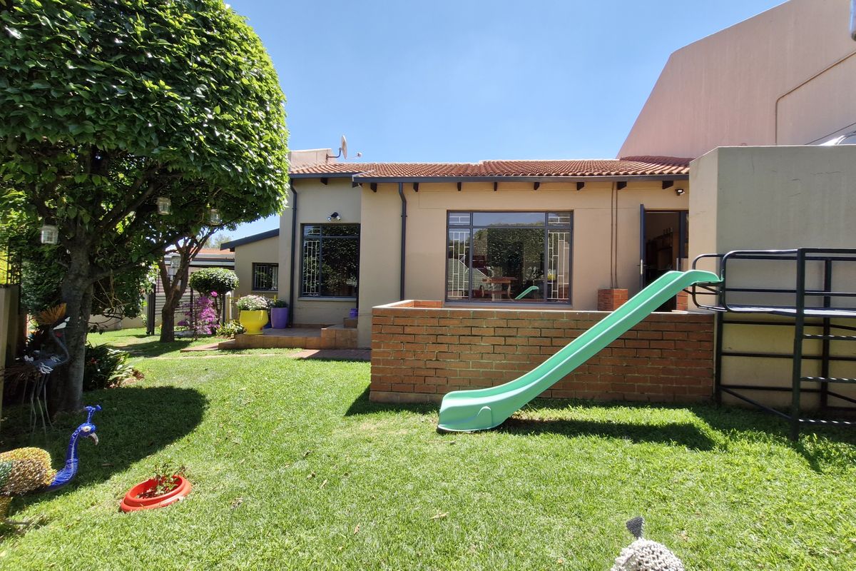 Rear view of the townhouse featuring a private garden, lawn area, and a brick retaining wall with access to the main dwelling.