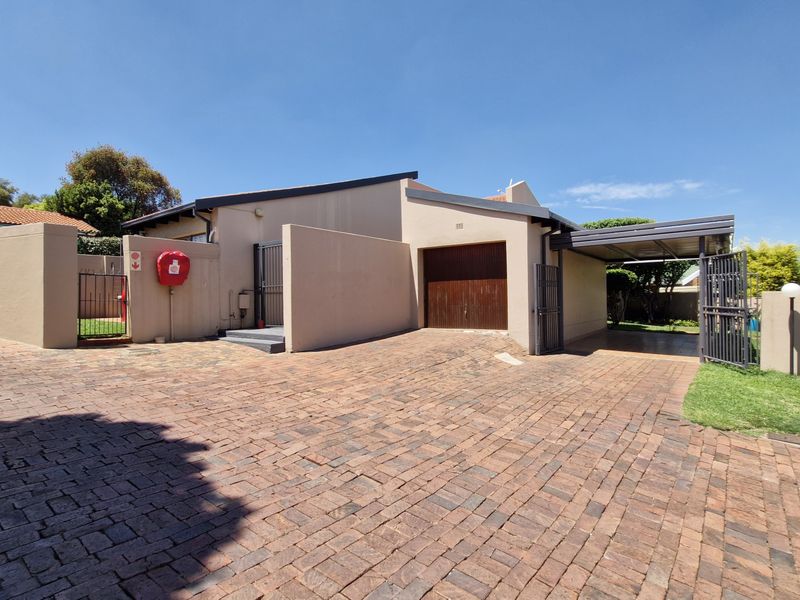 Front exterior view of the townhouse featuring a paved driveway, single garage, and an attached carport with secure boundary walling.