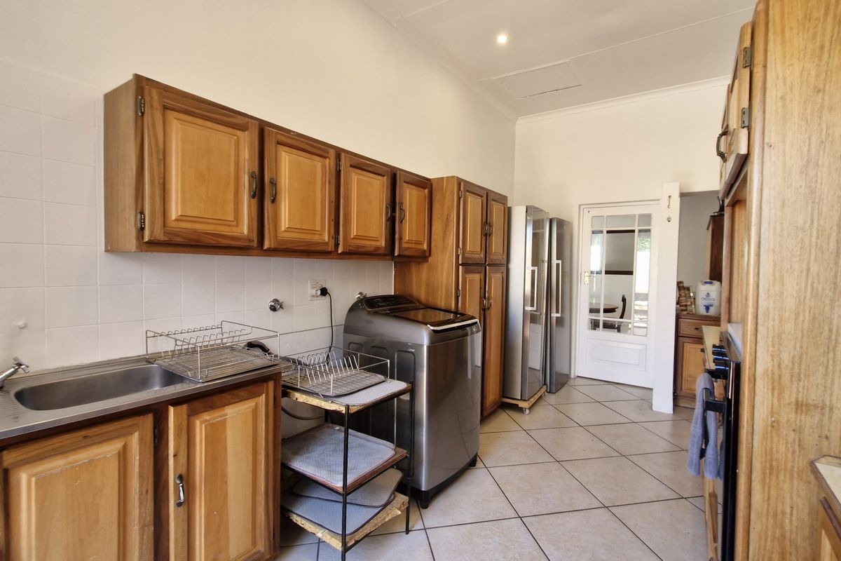 A functional kitchen featuring wooden cabinetry, tiled splashbacks, and tiled flooring, offering a practical layout with direct access to adjacent living areas.