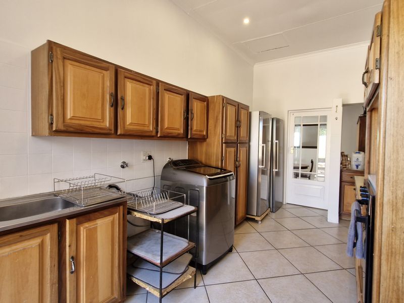 A functional kitchen featuring wooden cabinetry, tiled splashbacks, and tiled flooring, offering a practical layout with direct access to adjacent living areas.