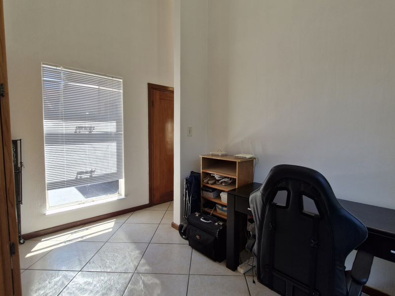 A bedroom featuring tiled flooring, high ceilings, and a window with venetian blinds, offering a functional space with potential for modernization.