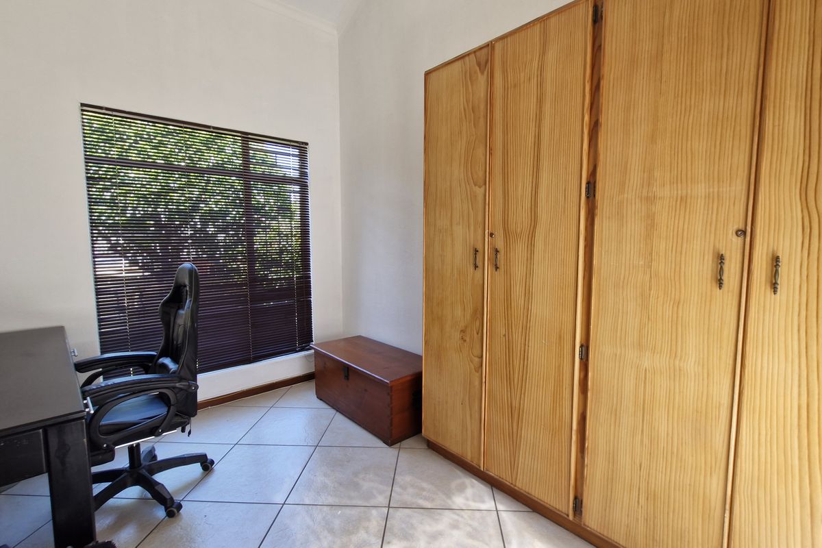 A bedroom featuring tiled flooring, a large built-in wooden wardrobe, and a window fitted with venetian blinds.