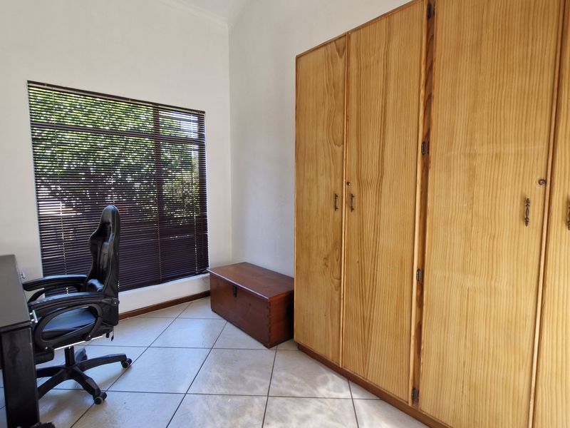 A bedroom featuring tiled flooring, a large built-in wooden wardrobe, and a window fitted with venetian blinds.