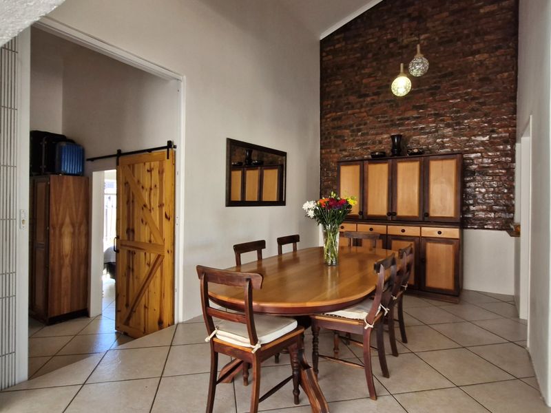 Dining area featuring a striking exposed brick feature wall, vaulted ceilings, and neutral ceramic floor tiles, creating a warm and inviting atmosphere.