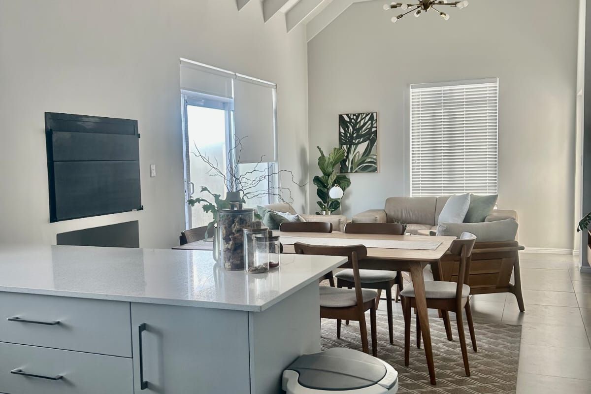 Spacious open-plan living and dining area featuring a high vaulted ceiling with exposed rafters, a modern kitchen island, and a built-in fireplace.