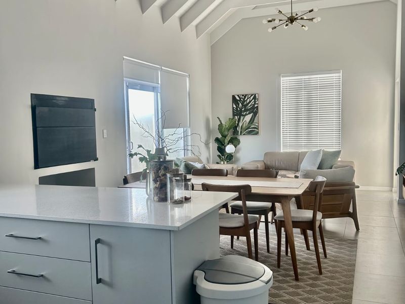 Spacious open-plan living and dining area featuring a high vaulted ceiling with exposed rafters, a modern kitchen island, and a built-in fireplace.