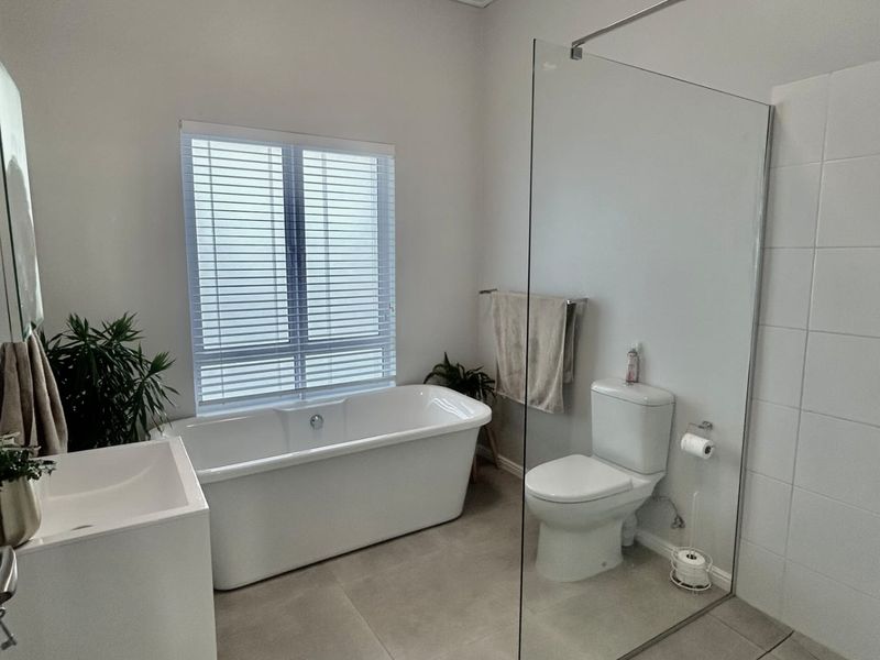 Modern bathroom featuring a freestanding bathtub, a spacious walk-in shower with a glass screen, and a wall-mounted vanity with neutral floor tiles.
