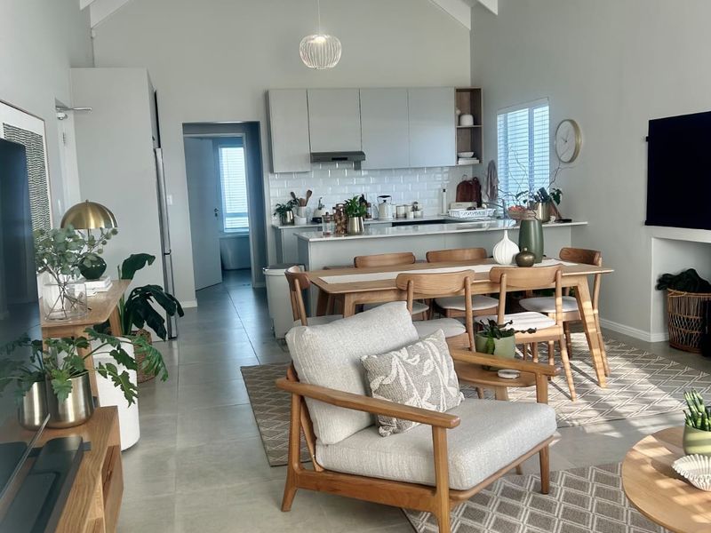 Spacious open-plan living and dining area featuring a high vaulted ceiling with exposed rafters, modern kitchen cabinetry, and neutral tiled flooring throughout.