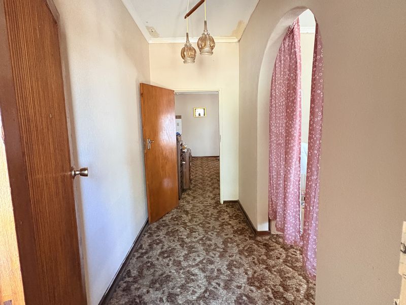 A dated hallway featuring an arched entryway, patterned carpet flooring, and visible ceiling wear, offering potential for modernization and cosmetic updates.