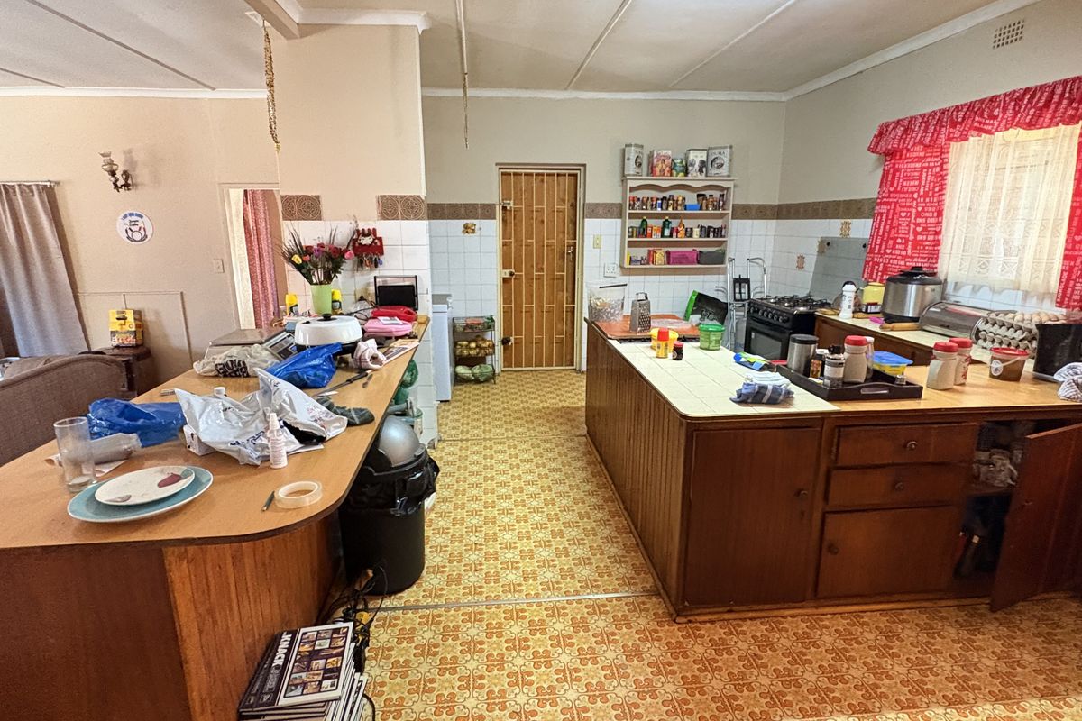 A dated kitchen featuring wooden cabinetry, tiled flooring, and a functional layout with a breakfast bar and built-in shelving.