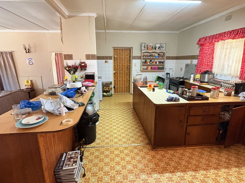 A dated kitchen featuring wooden cabinetry, tiled flooring, and a functional layout with a breakfast bar and built-in shelving.