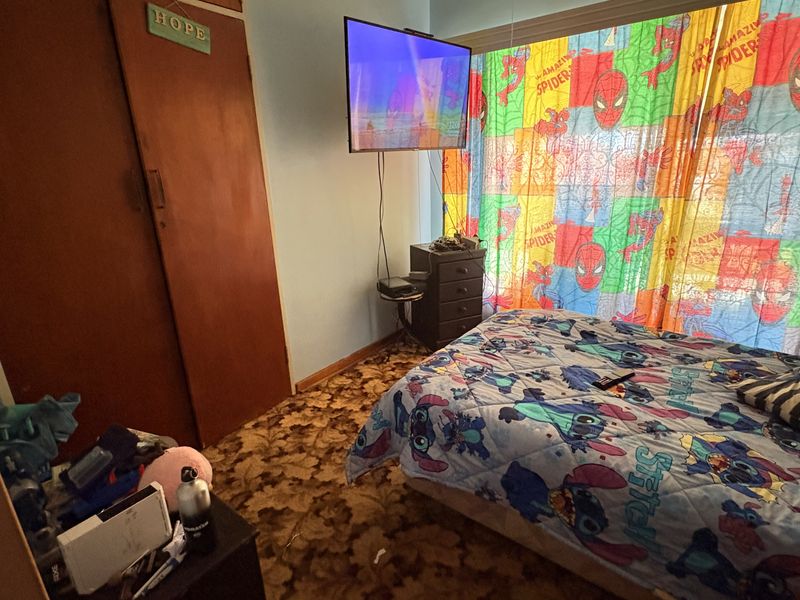 A bedroom featuring built-in wooden wardrobes, patterned carpet flooring, and a ceiling ventilation unit.