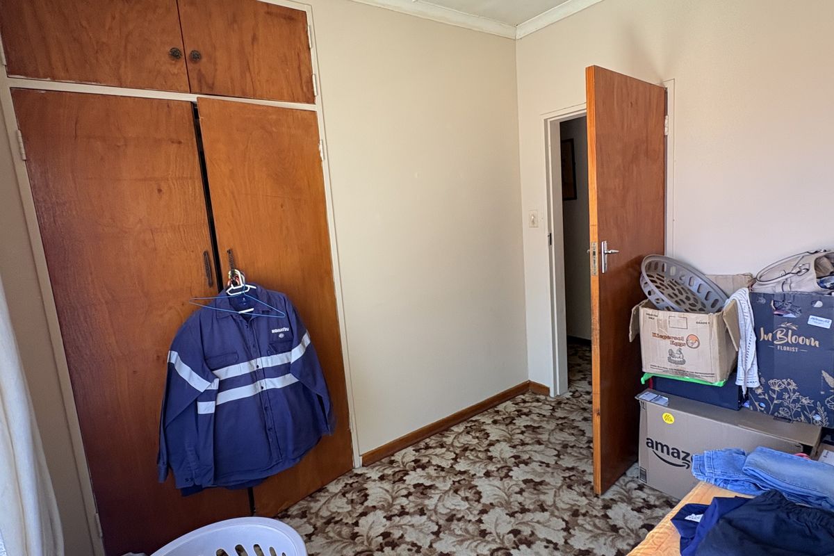 A bedroom featuring built-in wooden cupboards, patterned carpet flooring, and a standard wooden door, offering a functional space in need of cosmetic updates.