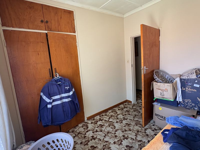 A bedroom featuring built-in wooden cupboards, patterned carpet flooring, and a standard wooden door, offering a functional space in need of cosmetic updates.