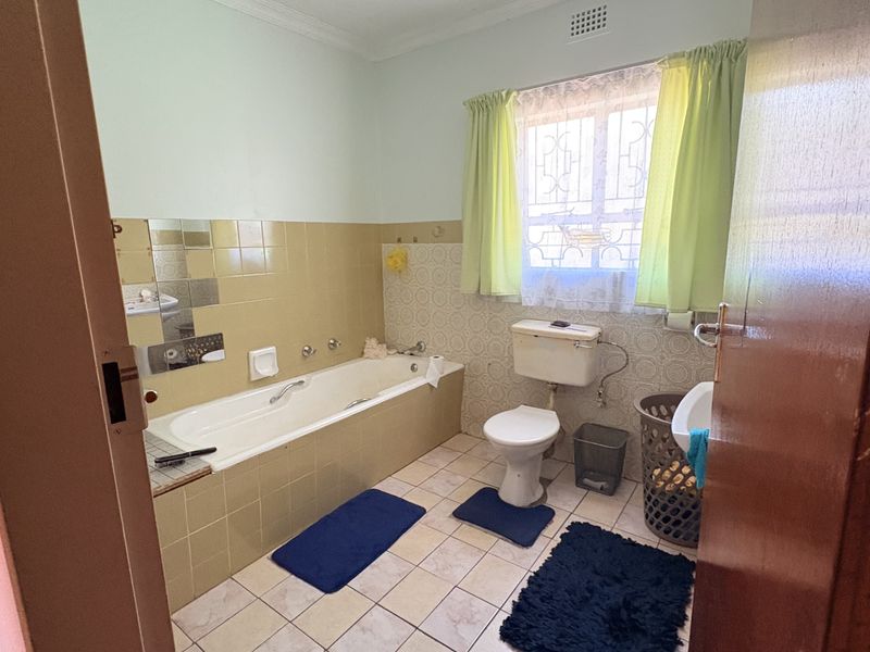 A functional bathroom featuring a built-in bathtub, pedestal basin, and toilet, finished with dated ceramic wall and floor tiles.