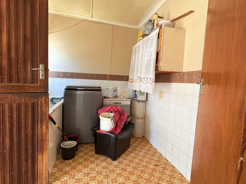 A functional laundry area featuring tiled flooring, wall tiling, and built-in cabinetry, offering a practical space for utility and washing needs.